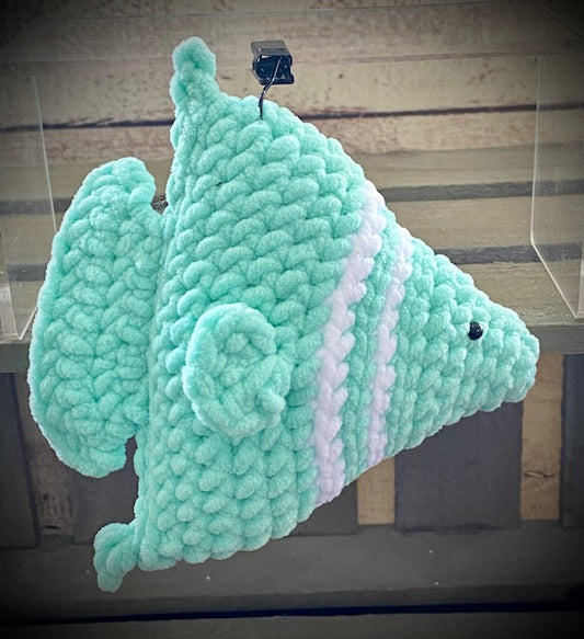 Hand-crocheted plush toy resembling an angelfish, made from a green plush yarn with pink accents, displayed against a wooden background.